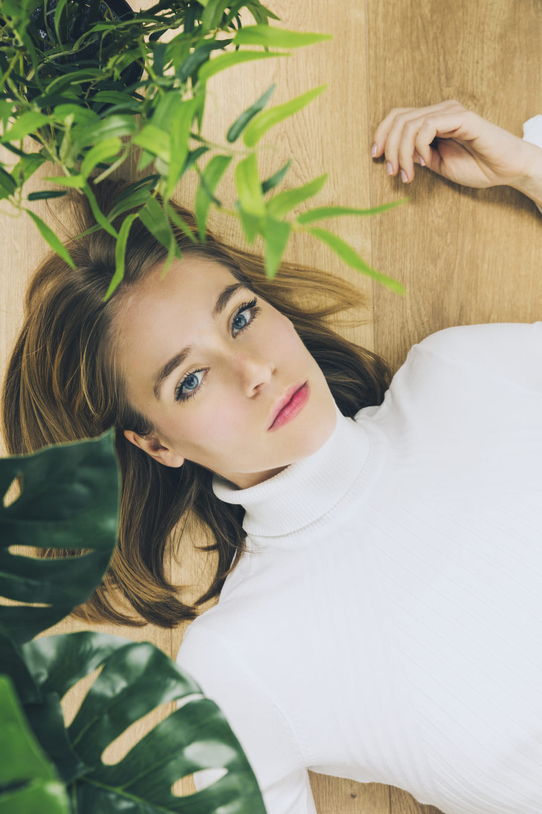 thoughtful-woman-lying-floor-near-green-plants